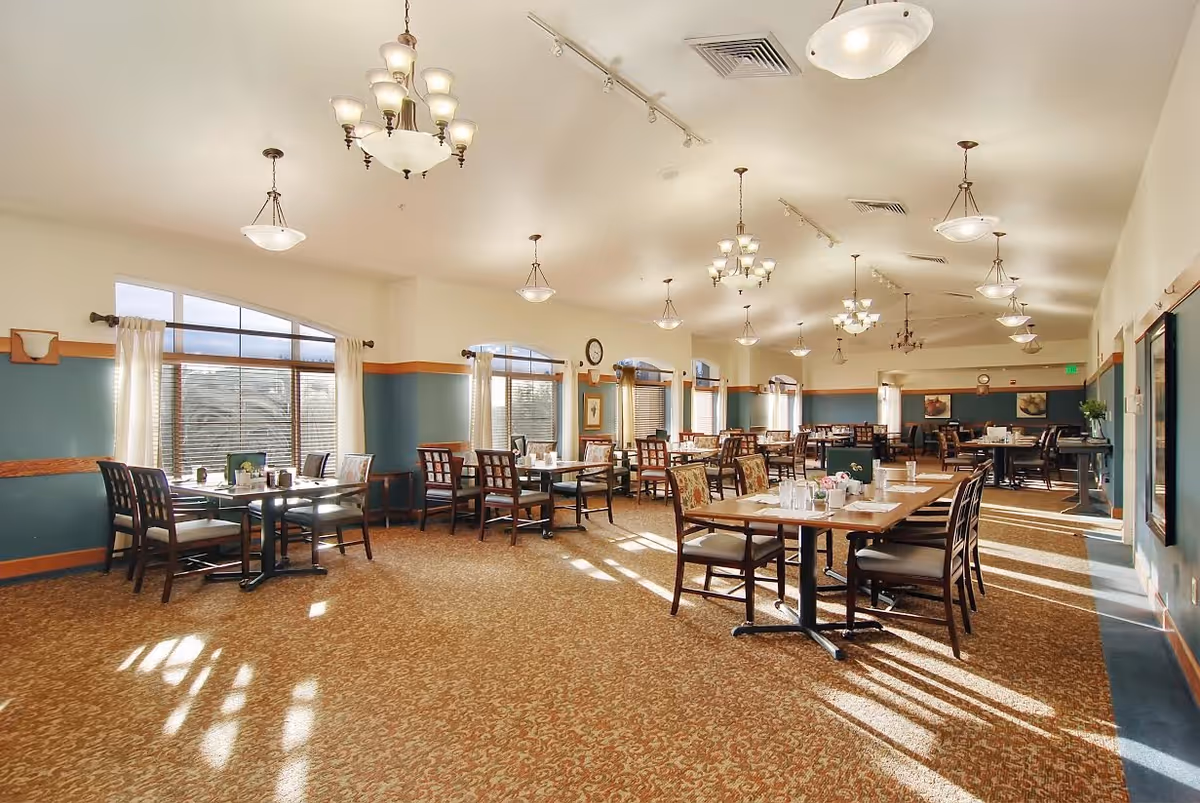 Spacious, well-lit dining room with multiple tables and chairs, large windows, and chandeliers.