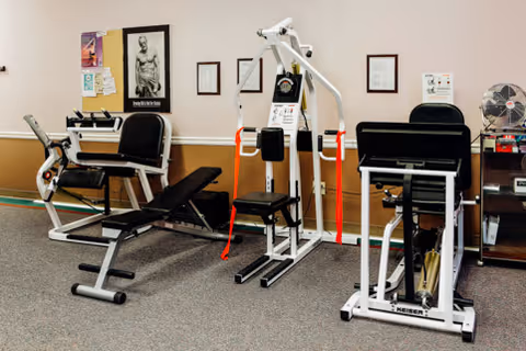 Exercise room with weight machines and benches against a beige wall.