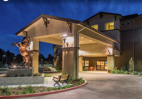 Exterior view of Carlton Senior Living Davis entrance with sculpture, bench, and dusk lighting