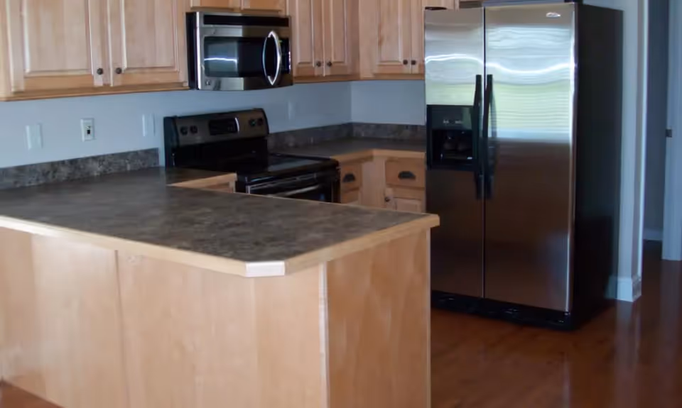 Open kitchen with wooden cabinets, a peninsula countertop, electric stove, microwave, and stainless steel refrigerator.