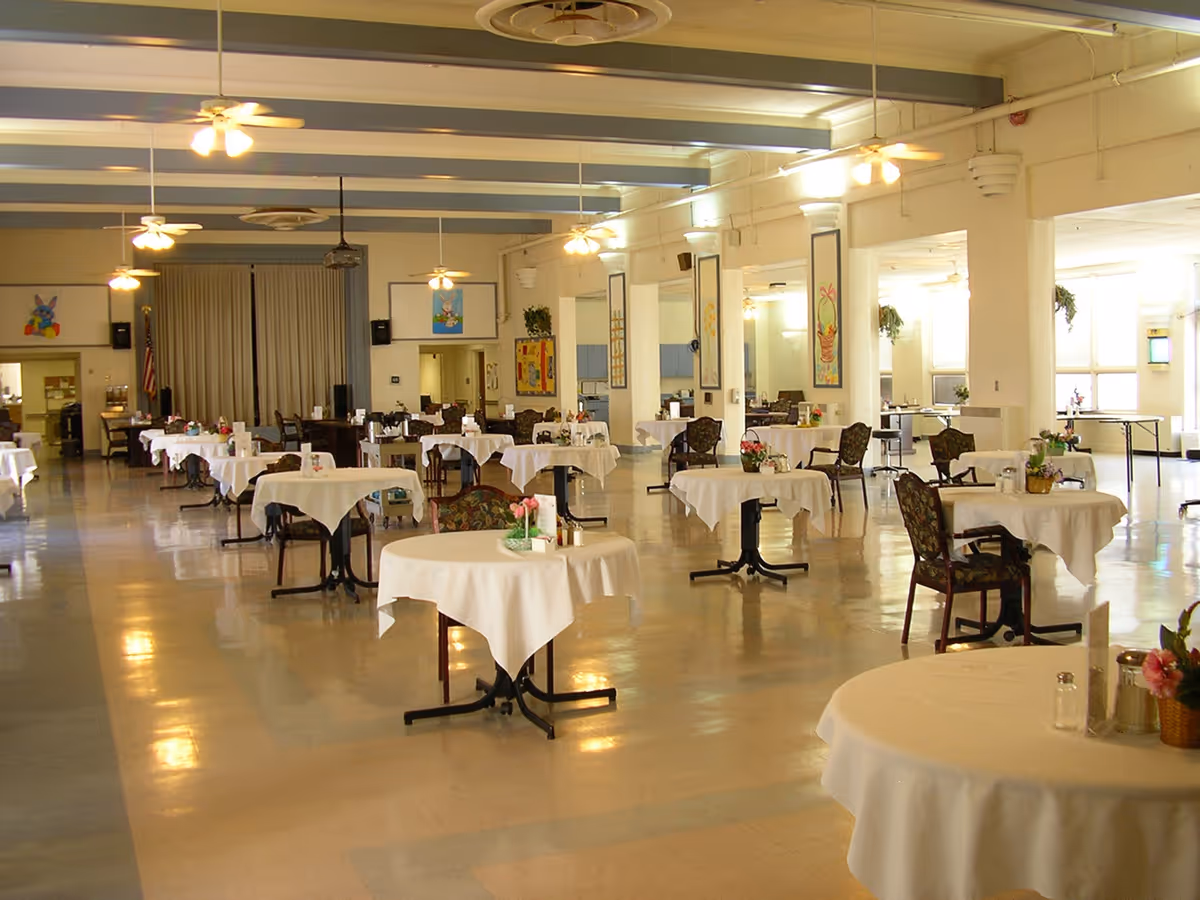 Large dining hall with multiple round tables covered in white tablecloths and floral centerpieces.