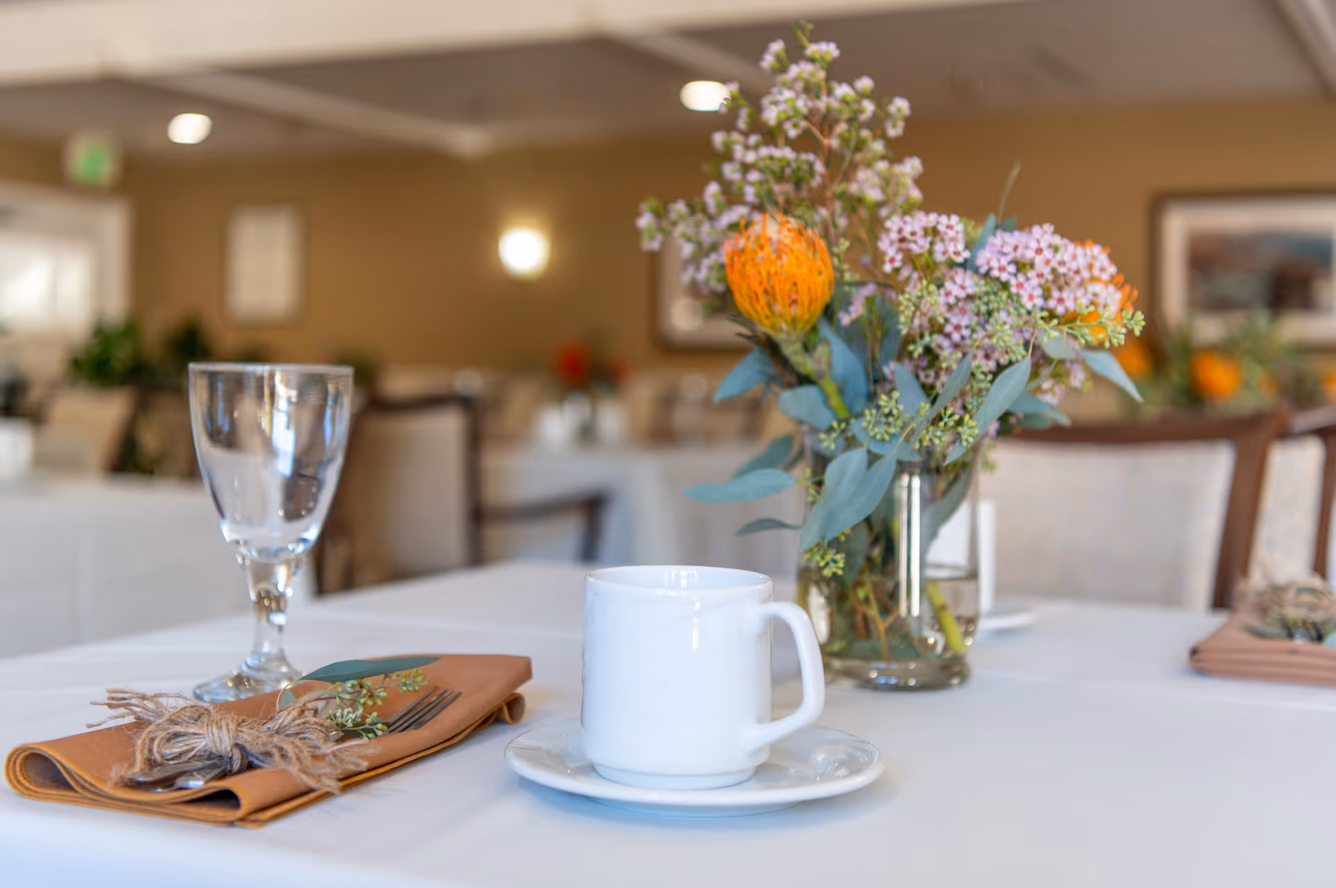 Table set with a coffee cup, wine glass, folded napkin and a floral centerpiece in a dining room.