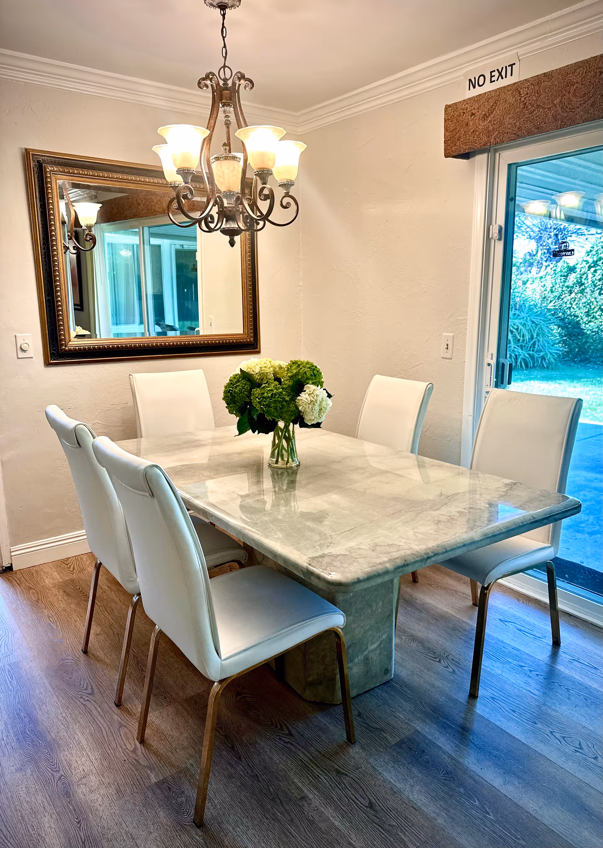White upholstered dining chairs surround a marble table in a bright dining room.