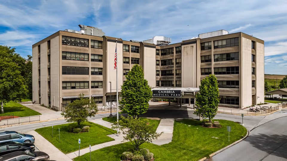Large beige medical building with central entrance, flagpole, and green lawn.