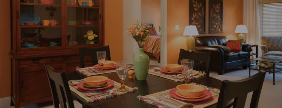 Dining table set for a meal in an open living and dining area of a senior living facility.
