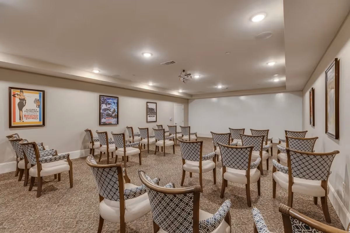 A medium-sized room set up with multiple rows of patterned chairs facing a blank white wall, likely for presentations or meetings. The walls are decorated with framed movie posters including Breakfast at Tiffany's, Rocky, and others. The room has recessed lighting and a carpeted floor.