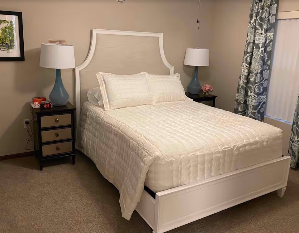 A cozy bedroom featuring a white quilted bedspread, bedside tables with lamps, and patterned curtains.