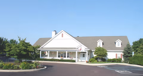 Single-story light-colored senior living facility with a covered front porch, landscaped beds, and a front parking area.