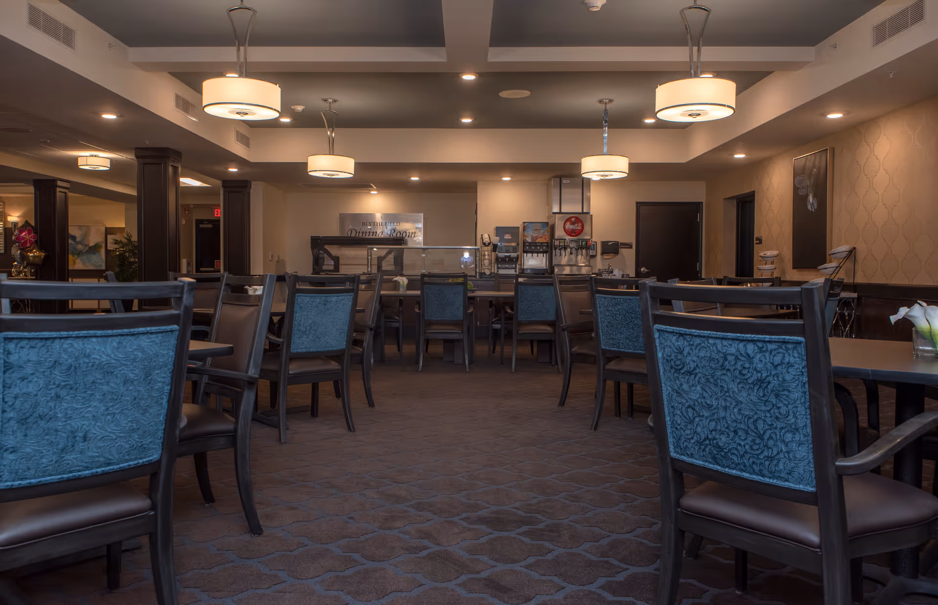 Spacious dining room with multiple tables and chairs, pendant lighting, and a beverage station at the back.