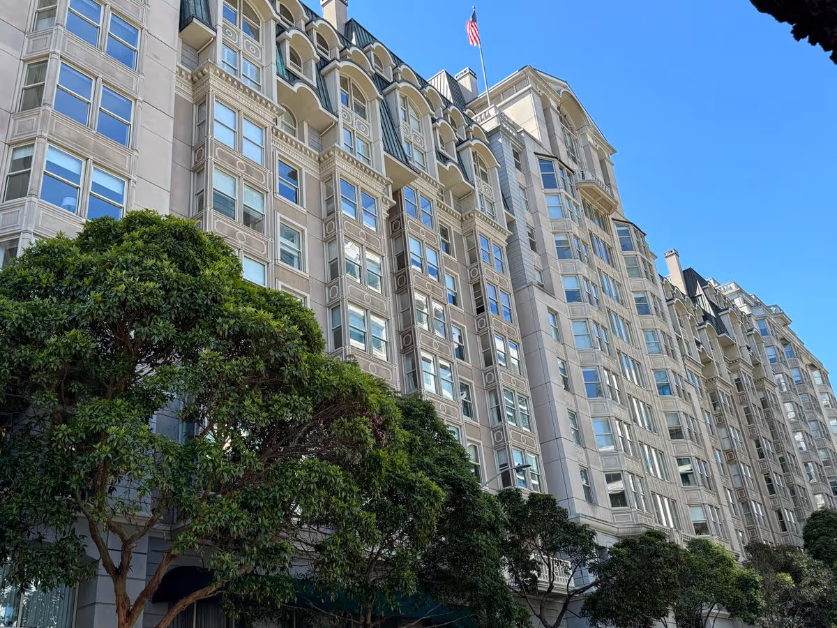 Exterior front facade of a multi-story residential building with trees and an American flag against a clear blue sky.