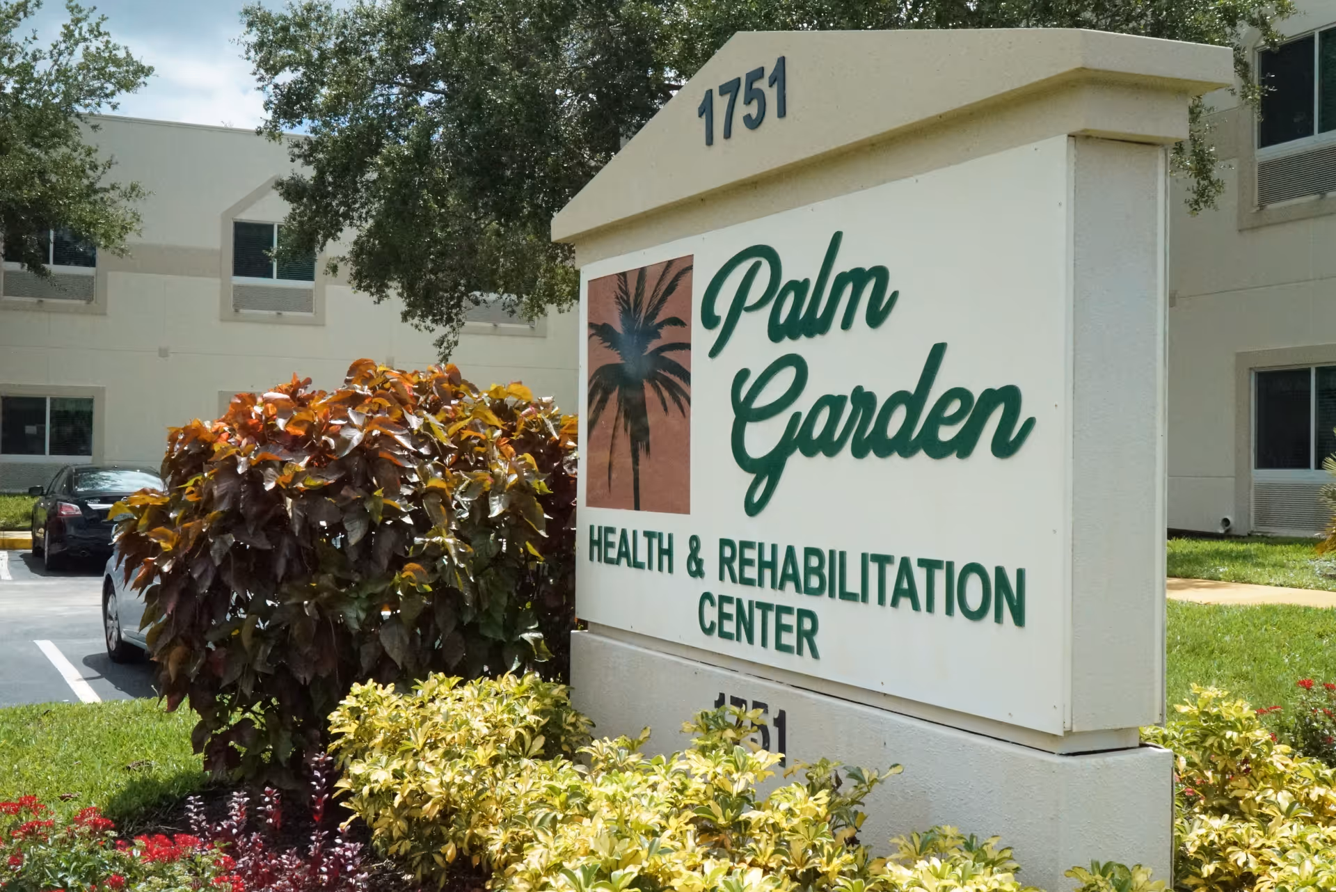 Sign for Palm Garden Health & Rehabilitation Center with landscaping and the facility building in the background.