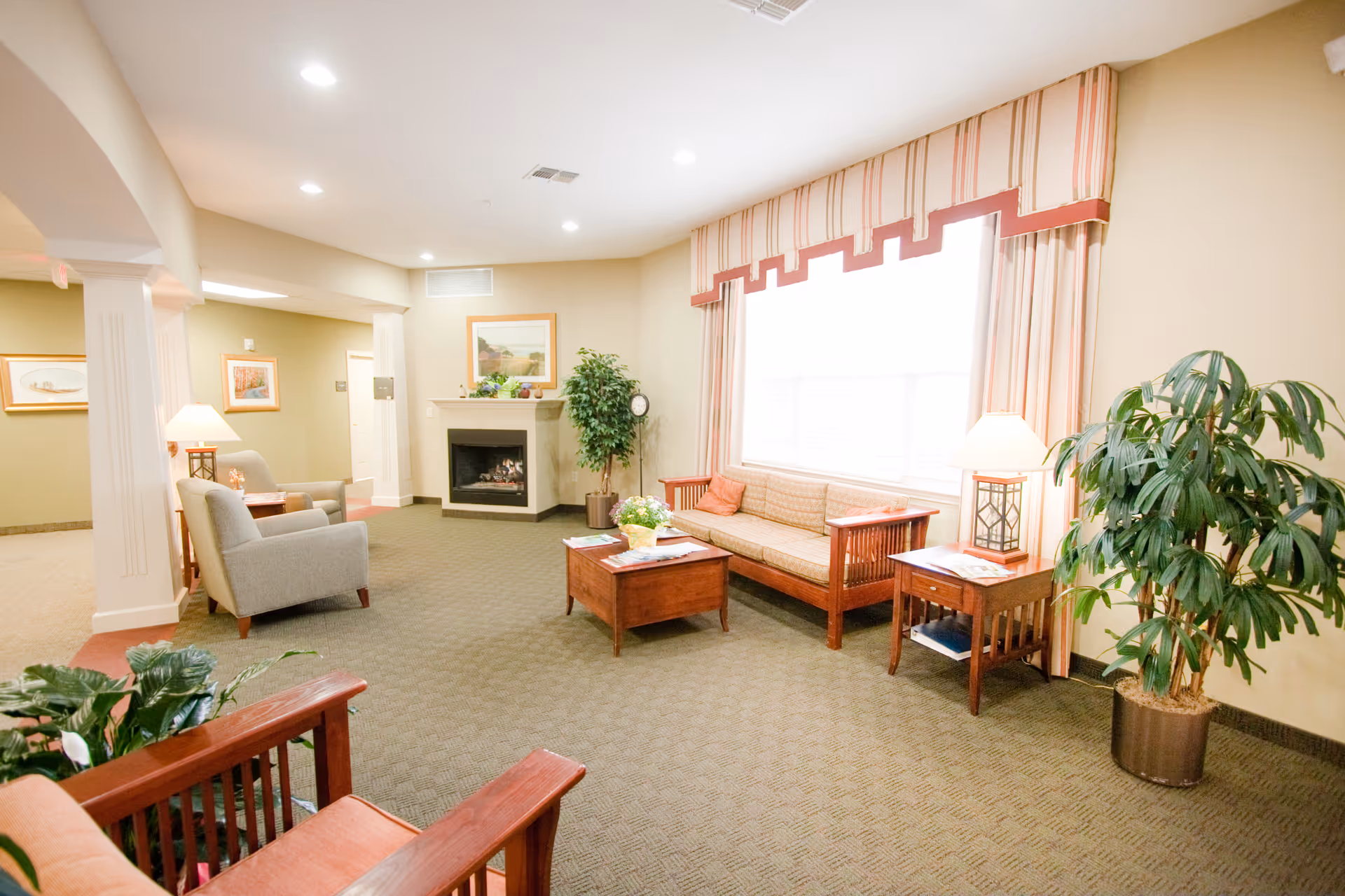 Bright communal living room with sofas, armchairs, coffee table, fireplace and a large curtained window.