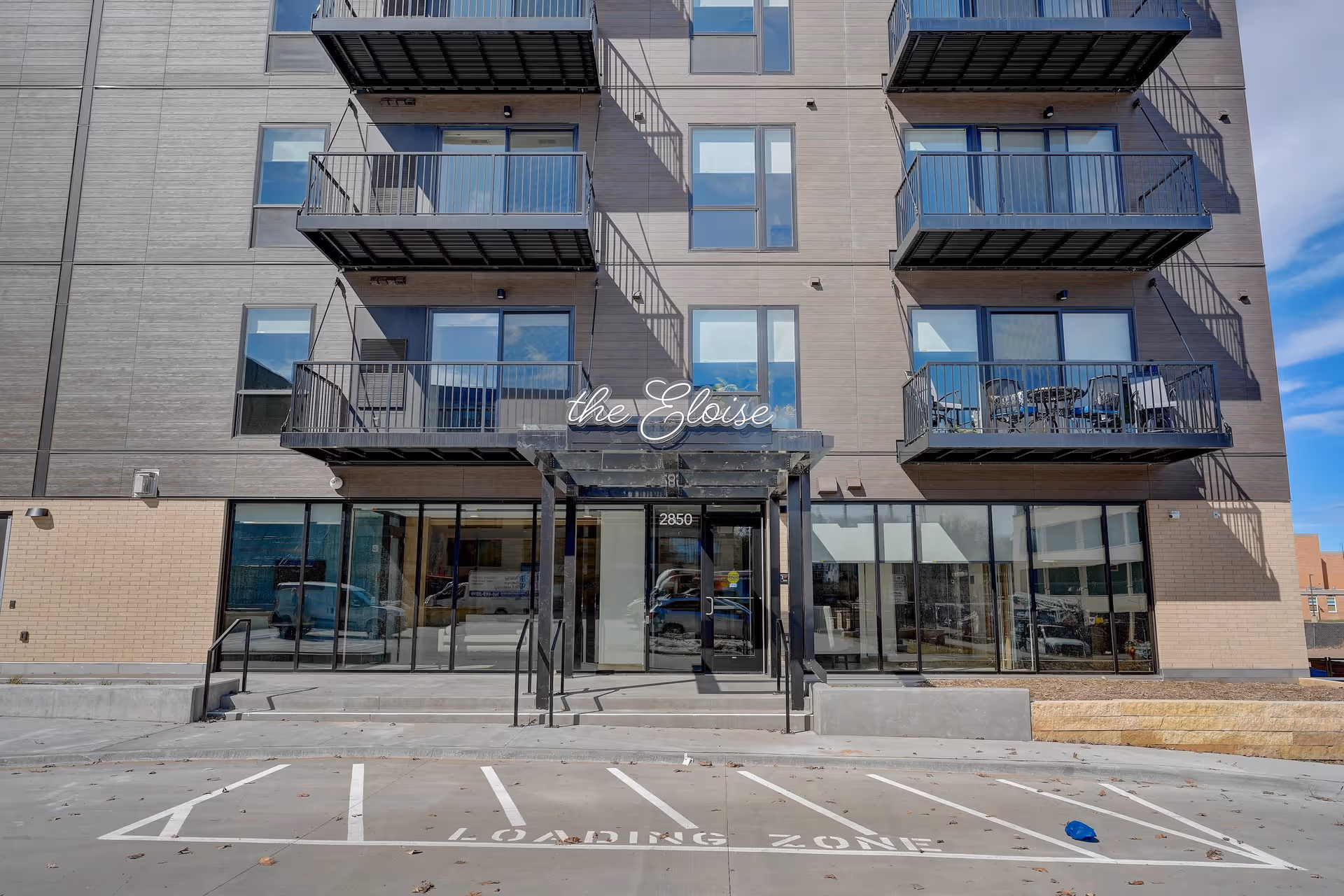 Front exterior view of a modern multi-story building named 'the Eloise' with balconies and a glass entrance door. There is a loading zone marked on the pavement in front of the entrance.