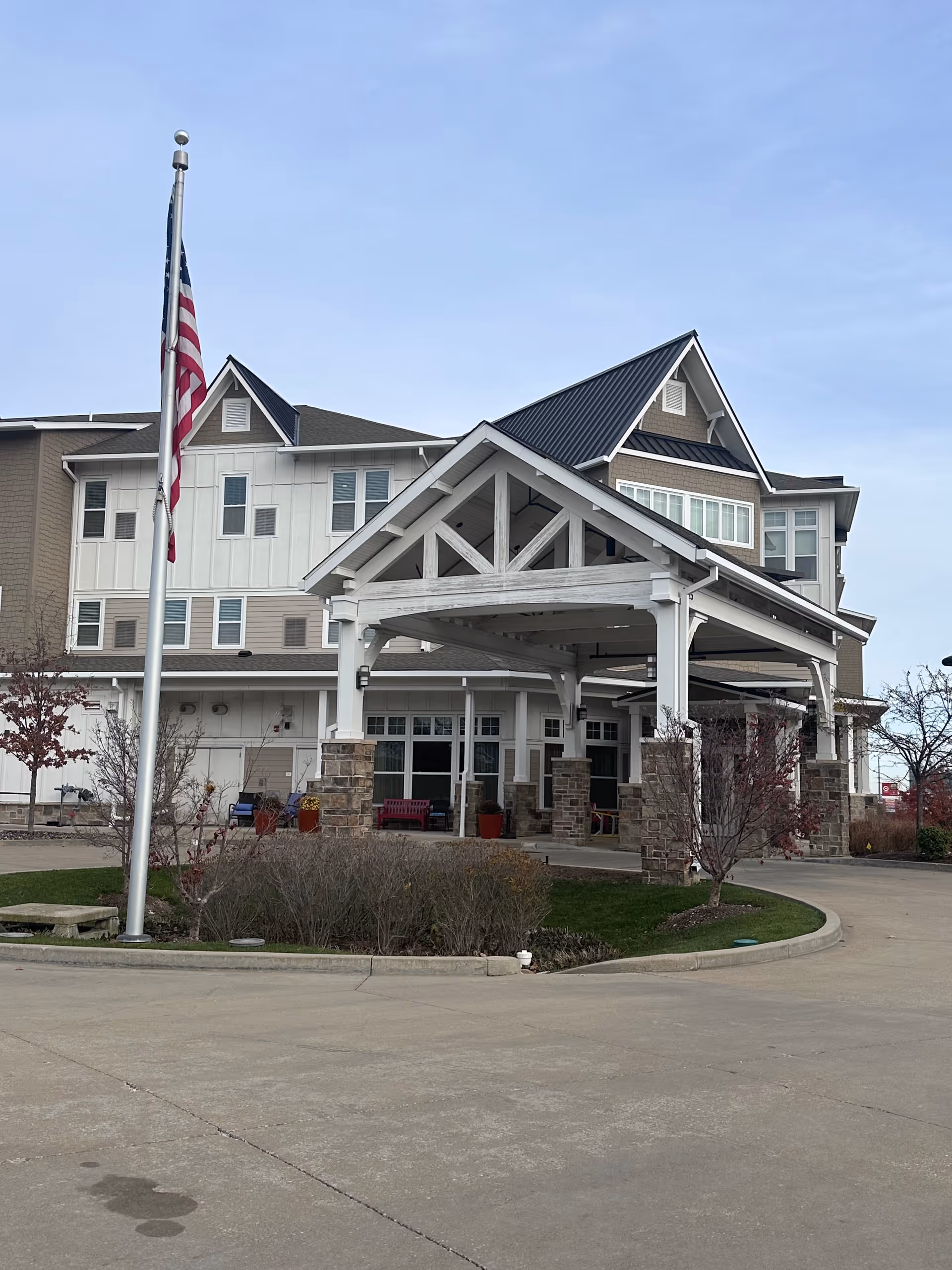 Front entrance of Promenade Senior Living with a covered porte-cochere, American flag, and landscaped driveway.