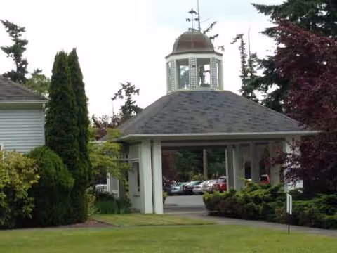 Front view of a covered entrance with a cupola, greenery, and parked cars nearby.
