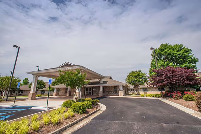 Front entrance of a single-story healthcare building with a covered drop-off canopy, driveway, handicap parking spaces, and landscaped beds.