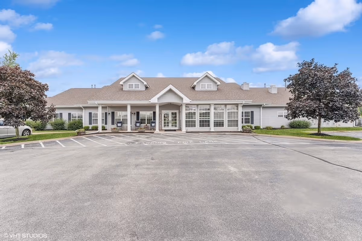 Front exterior view of Digby Place facility showing a single-story building with a pitched roof, large windows, a covered entrance with columns, and a parking lot in front. There are two trees on either side of the building and a clear blue sky with some clouds above.