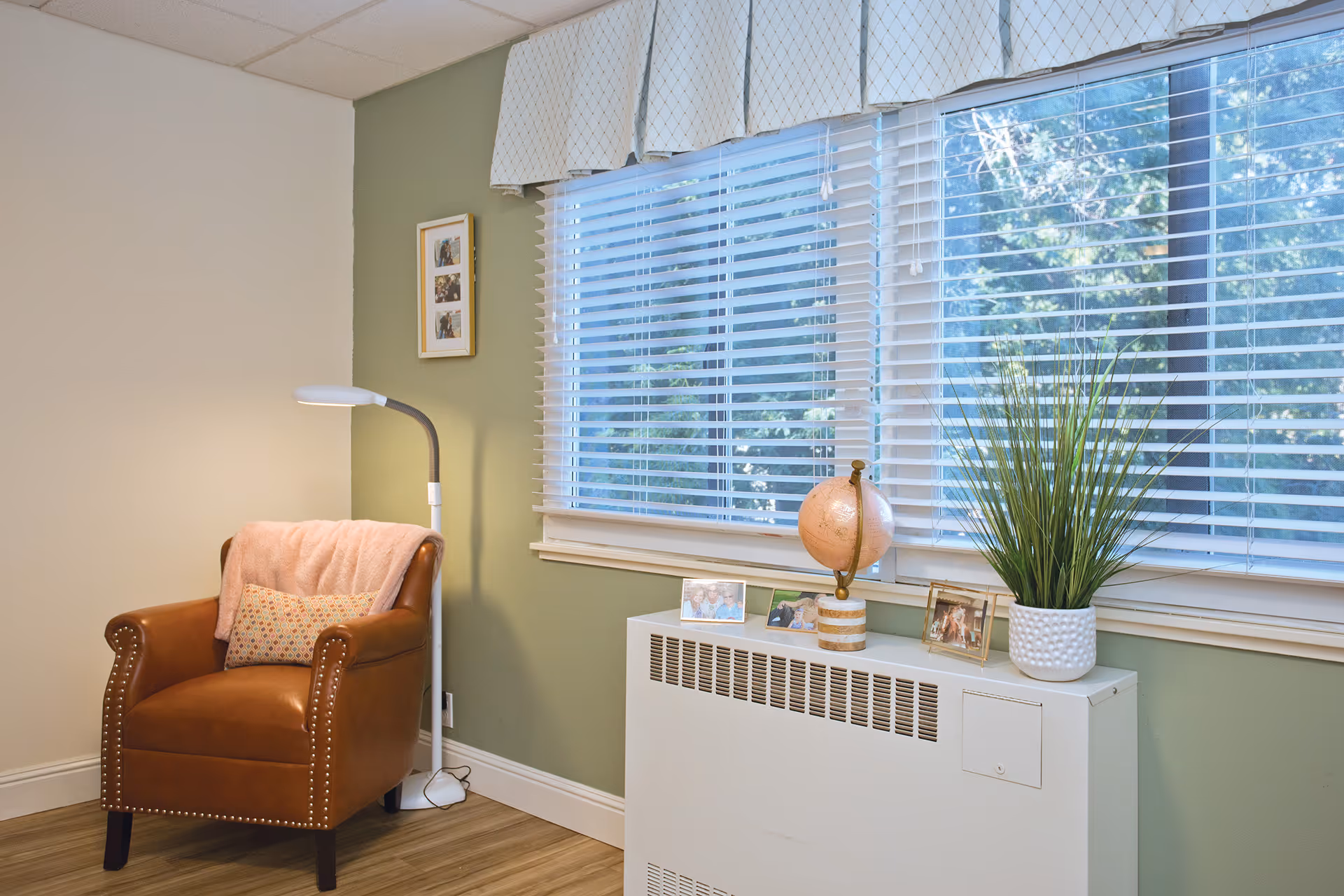 A cozy seating corner with a leather armchair, floor lamp, and a window sill holding a globe, plant, and framed photos.