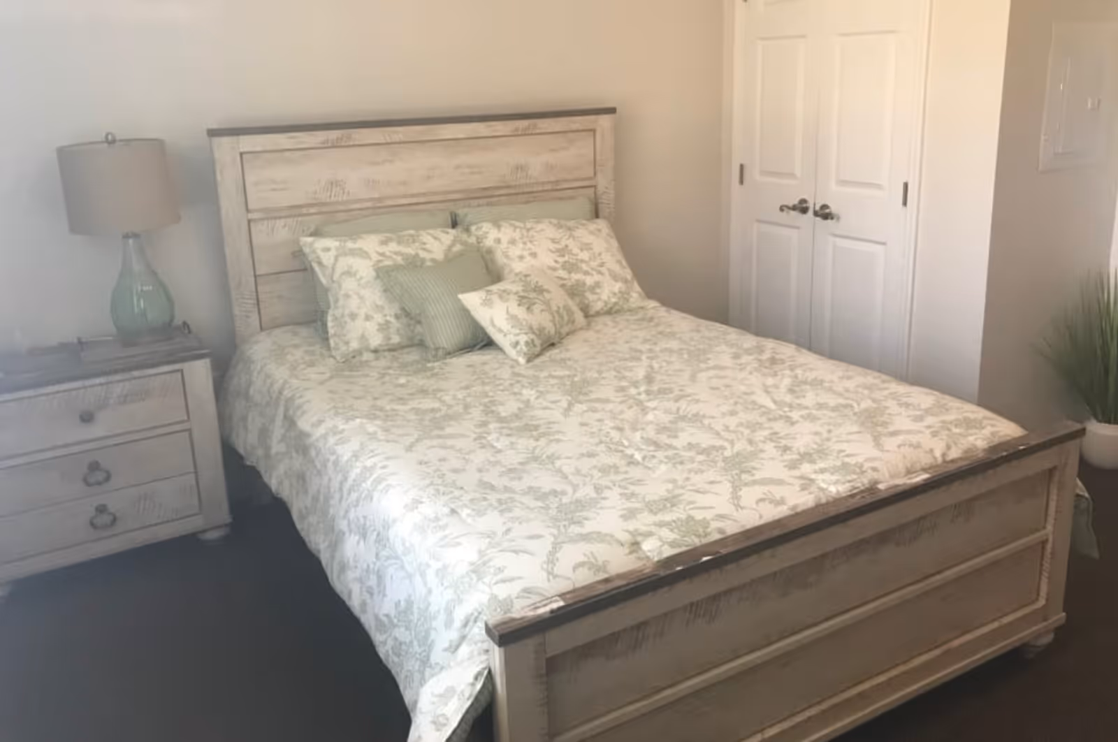Bedroom with a wooden bed dressed in light floral bedding, a nightstand with a lamp, and double closet doors.