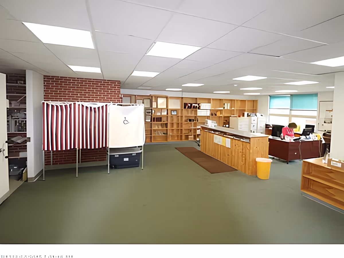 Spacious interior common area with a long wooden reception desk, shelving, striped privacy booths and office workstations.