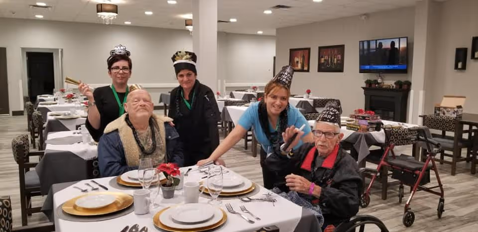 A dining room with set tables where staff and residents wearing party hats pose together around a table.