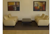 A seating area with four beige armchairs arranged around a low dark coffee table under two abstract paintings on the wall.