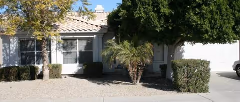 Front view of a single-story assisted living home with desert landscaping, shrubs, and a palm tree.