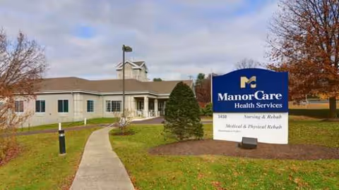 Exterior view of a nursing facility with a blue ManorCare sign and a walkway.