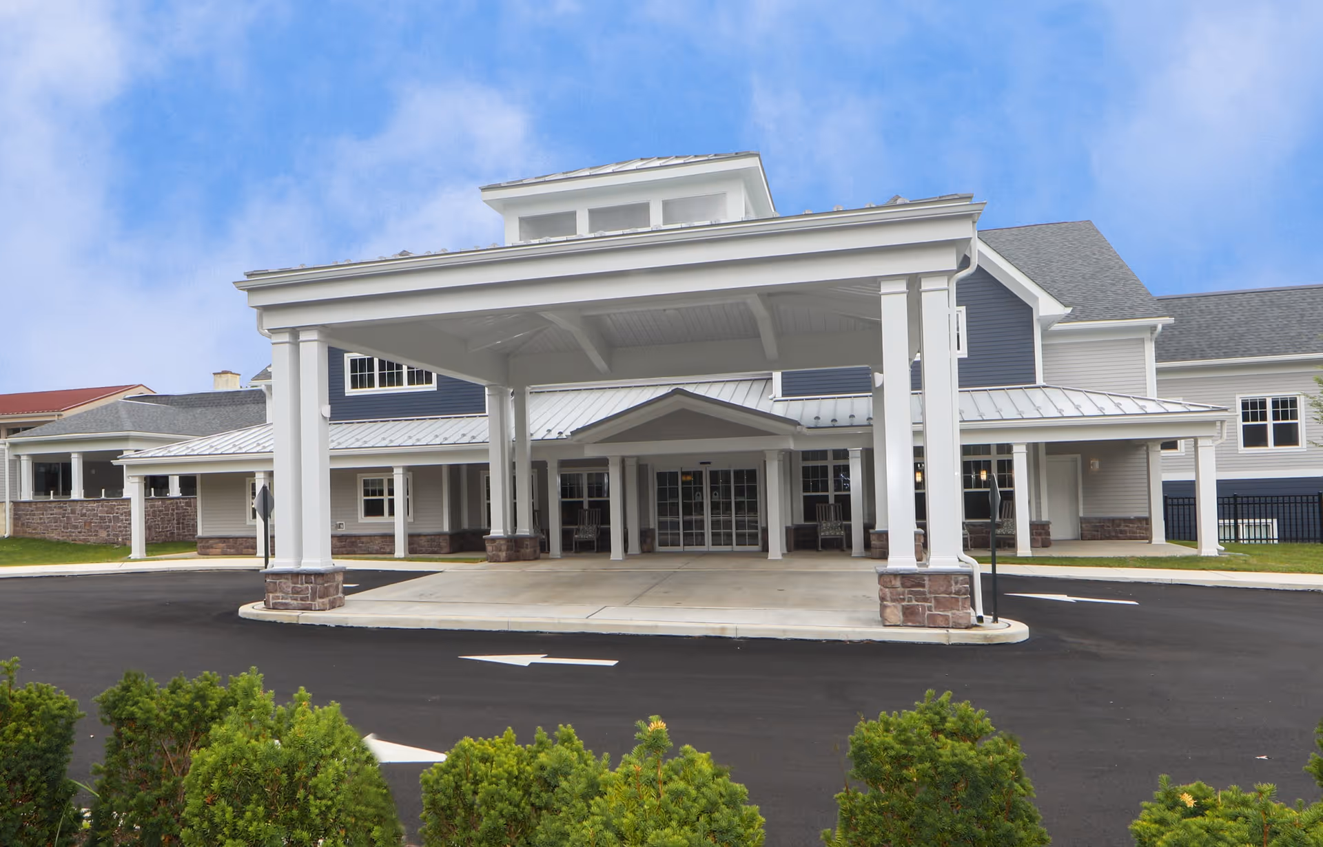 Front entrance with a large covered porte-cochère supported by columns at a two-story senior living building.