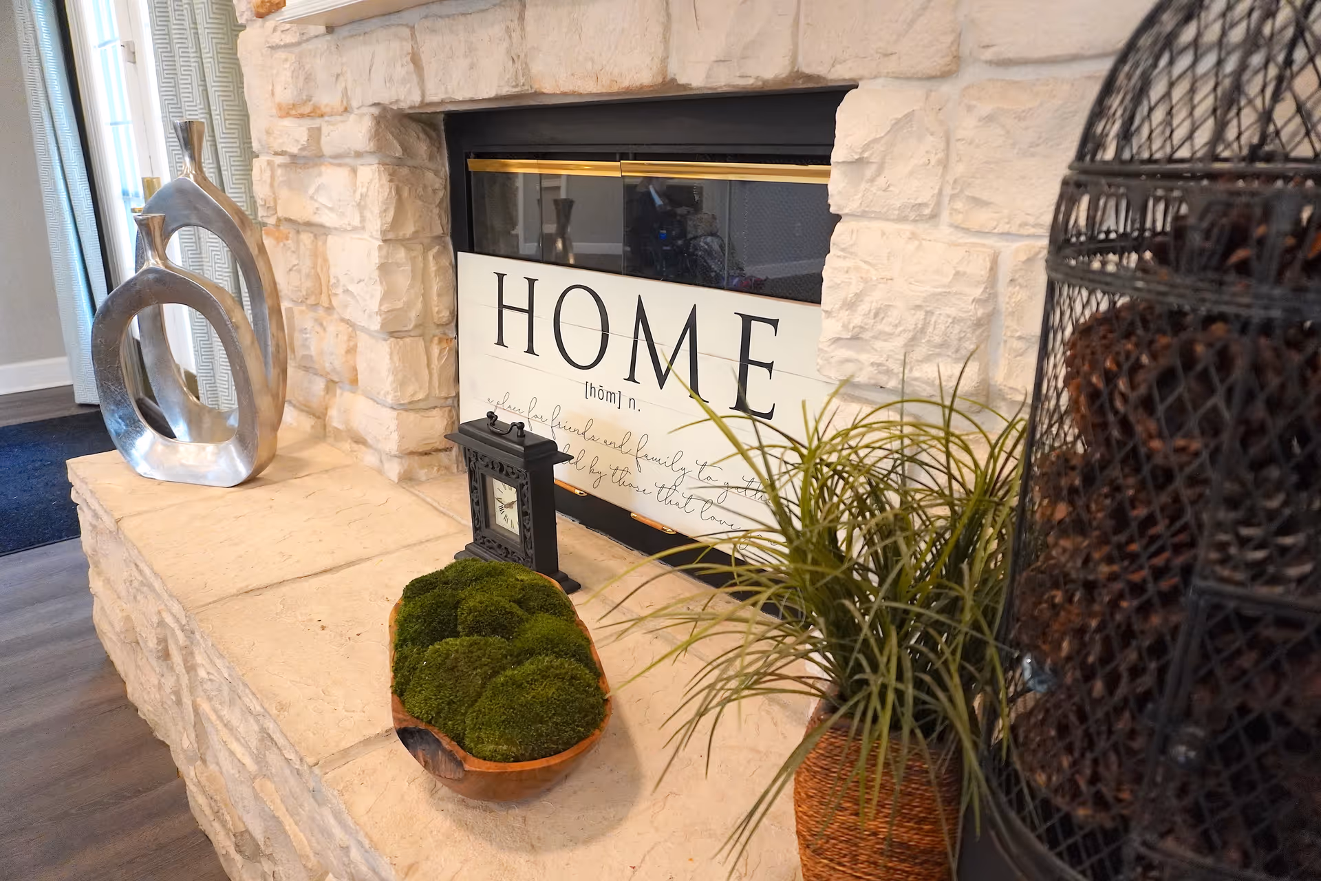 Stone fireplace mantel decorated with a 'HOME' sign, decorative sculptures, plants, and a small clock.