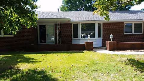Front exterior of a single-story brick senior living building with a grassy yard.