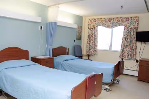 Two hospital-style beds in a nursing home patient room with blue sheets.