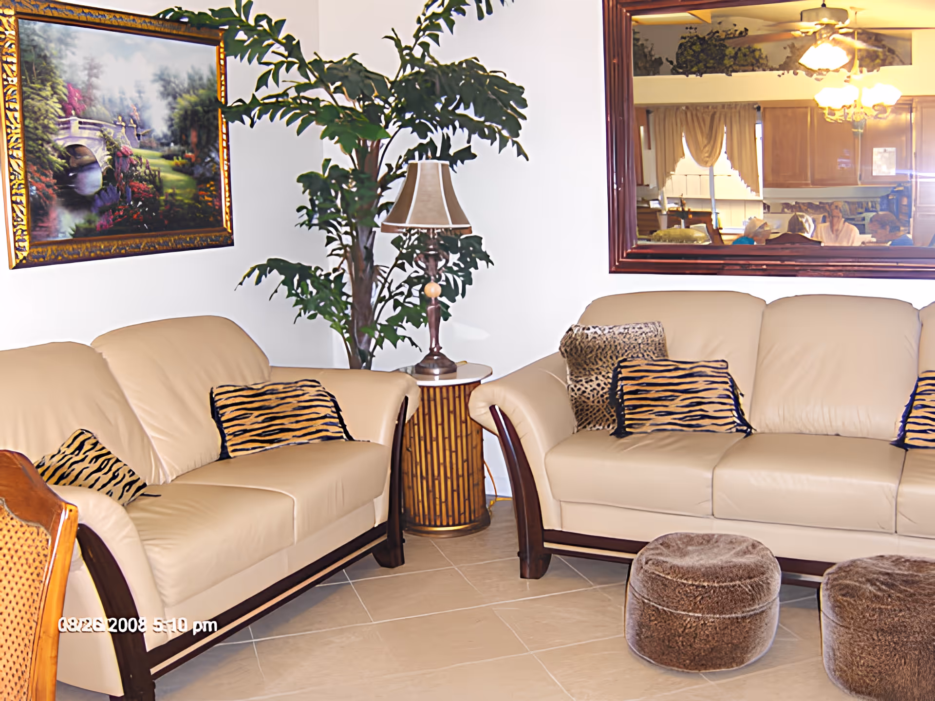 Bright living room with beige leather sofas, patterned throw pillows, a potted plant, lamp and a large wall mirror.