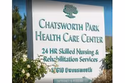 Outdoor sign for Chatsworth Park Health Care Center with text indicating 24 HR Skilled Nursing & Rehabilitation Services, located at 1610 Owensmouth. The sign is surrounded by greenery and trees under a clear blue sky.