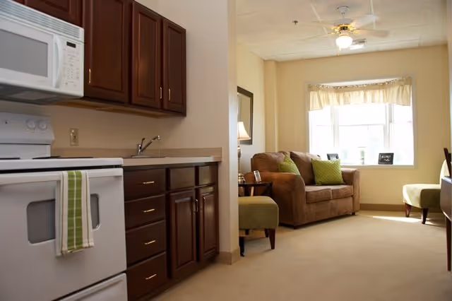 Small apartment-style interior with a kitchenette on the left and a cozy living area with a couch and window on the right.