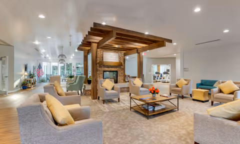 Spacious indoor common lounge with multiple sofas and chairs arranged around a central fireplace under a wooden pergola.