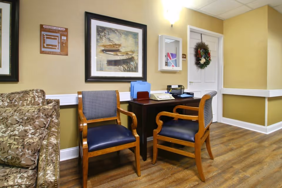 Small seating area with two wooden chairs and a desk against a wall decorated with framed art and a wreath.