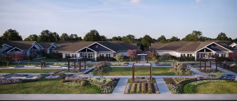 Wide view of a senior living facility named Larkspur at Shadow Creek featuring single-story buildings with pitched roofs surrounded by landscaped gardens, pathways, and pergolas under a clear sky.