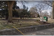 Outdoor view of Altenheim facility with lawn, trees, stone wall, and sign.