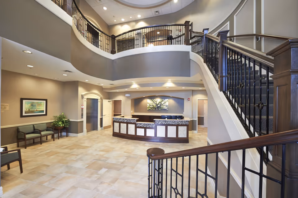 Spacious senior living lobby with a reception desk, curved staircase, seating area and second-floor balcony.