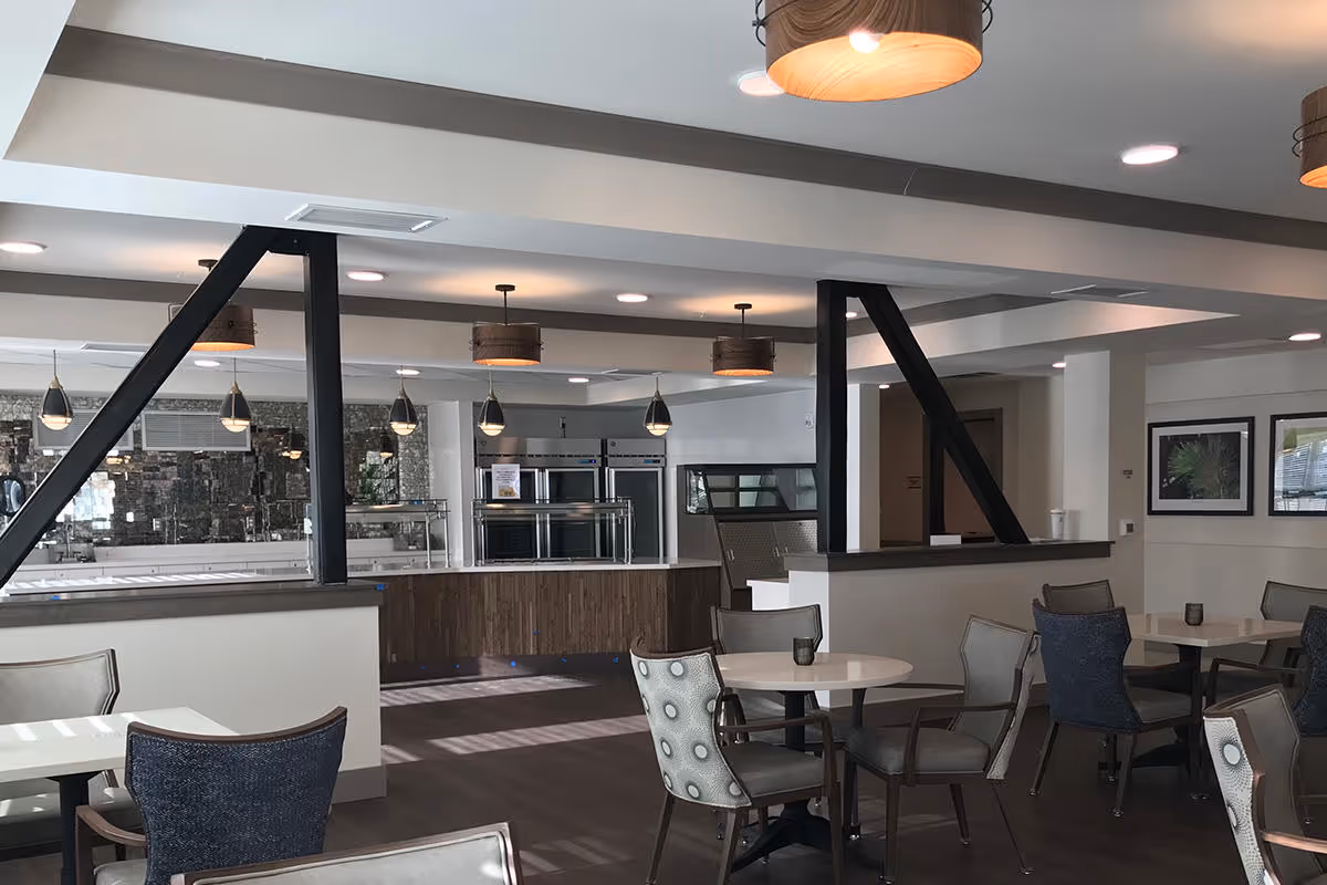 Open dining room with round tables and chairs facing a serving counter and pendant lights.