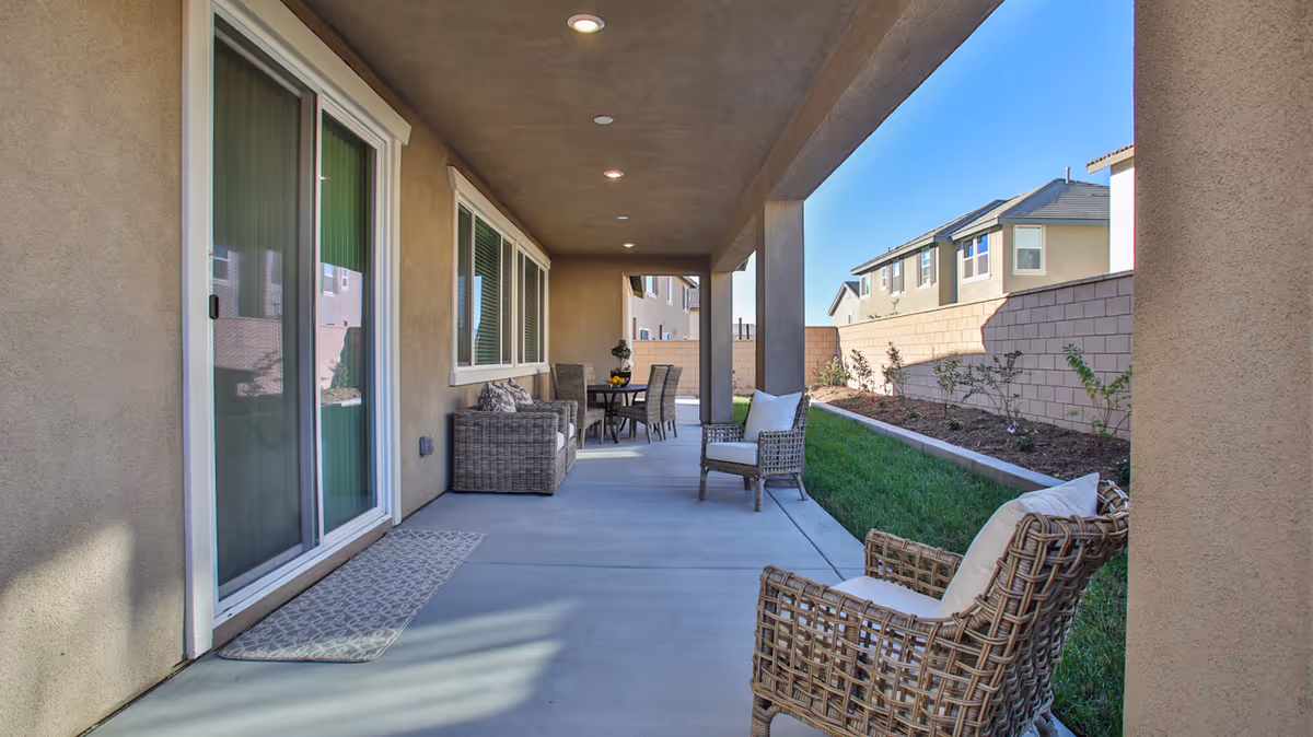 Covered patio with wicker chairs and a dining table next to sliding glass doors overlooking a small fenced backyard.