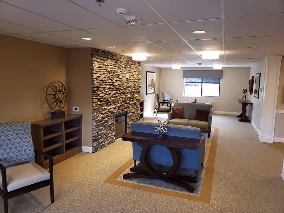 Well-lit communal living room with sofas, chairs, decorative table and a stone fireplace wall.