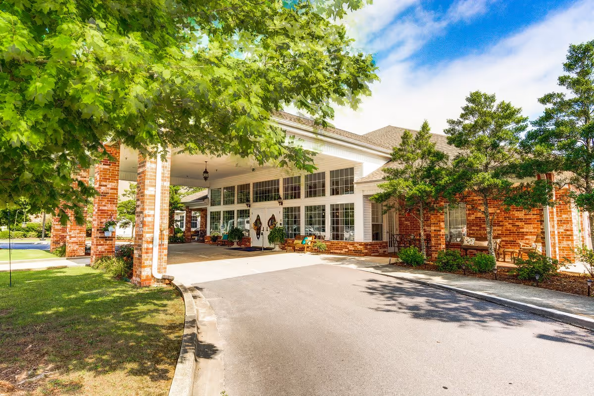 Front exterior view of a senior living facility named The Renaissance of Florence showing a covered entrance with brick pillars, large windows, and surrounding greenery under a partly cloudy blue sky.