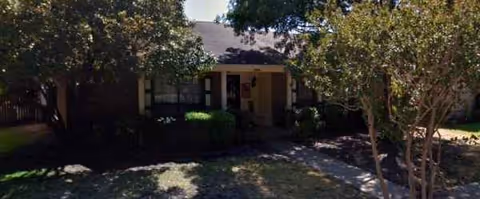 A single-story assisted living building with a front yard and surrounding trees.
