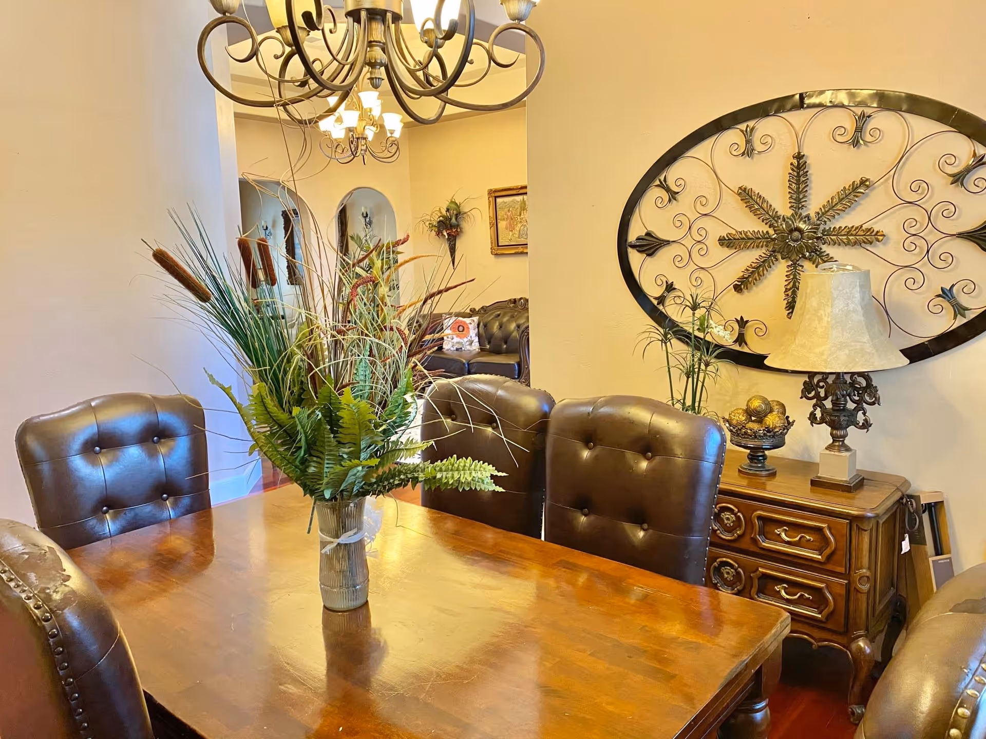 Dining room with a wooden table, tufted leather chairs, central floral arrangement, chandelier, and decorative wall art.