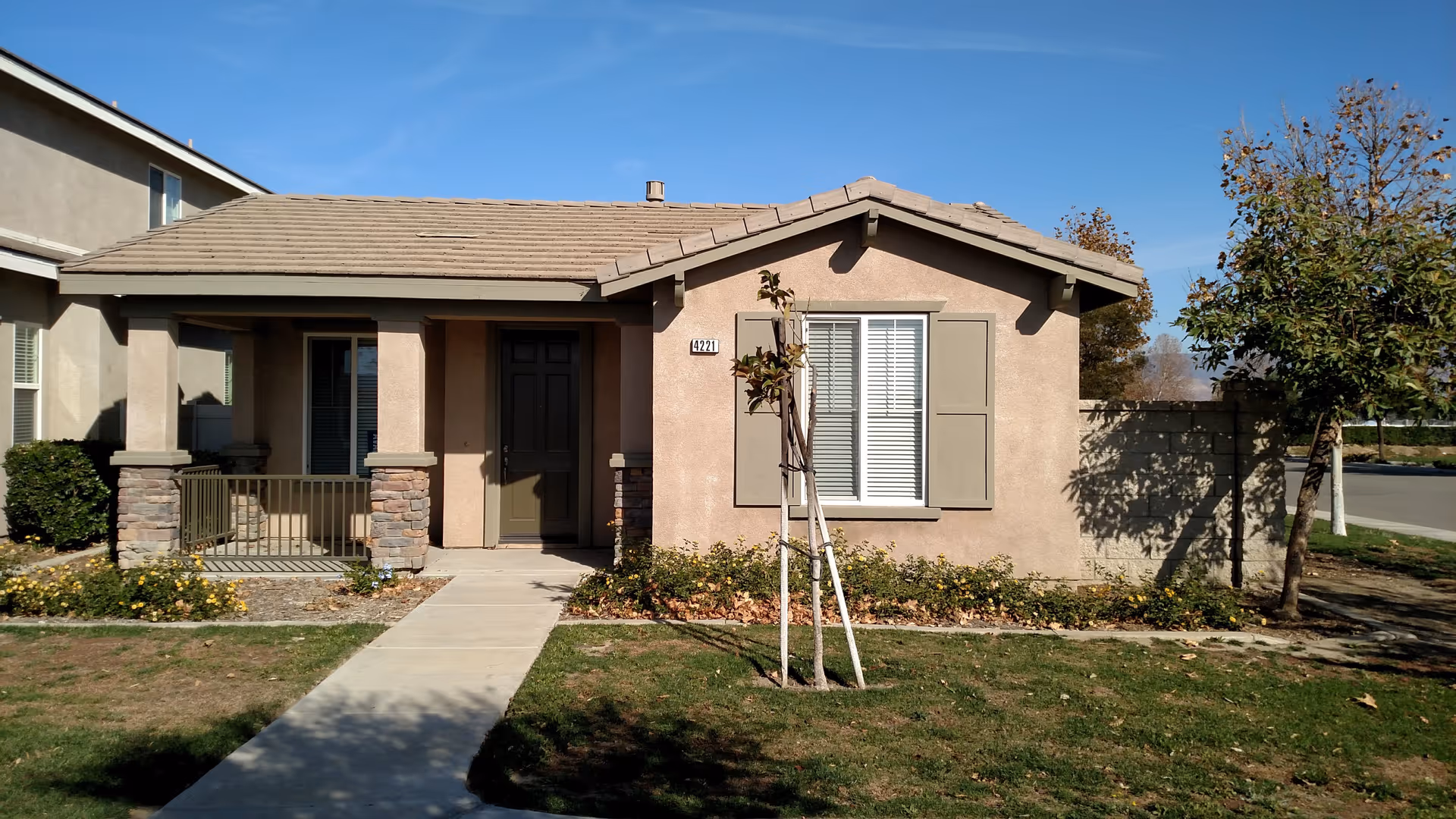 Single-story residential unit with a small front porch, walkway, and landscaped yard under a clear blue sky.