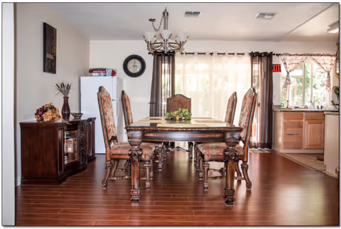Ornate wooden dining table with chairs beneath a chandelier in a spacious senior living dining room.