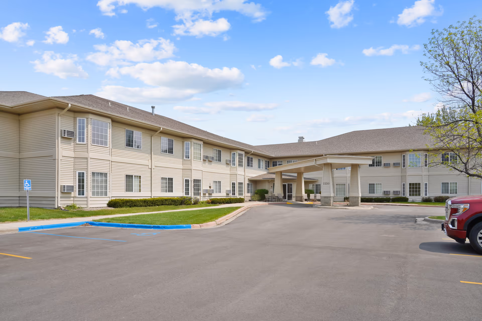Front exterior of a two-story beige senior living building with a covered entrance and adjacent parking lot.