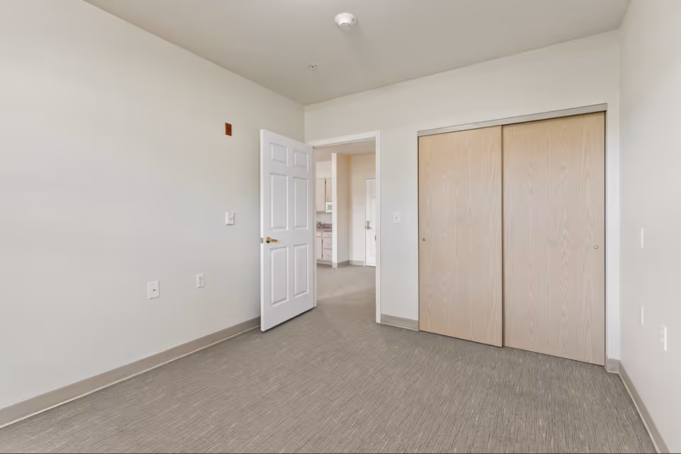 Empty neutral-toned bedroom with a sliding wood-door closet and an open door leading to a hallway.